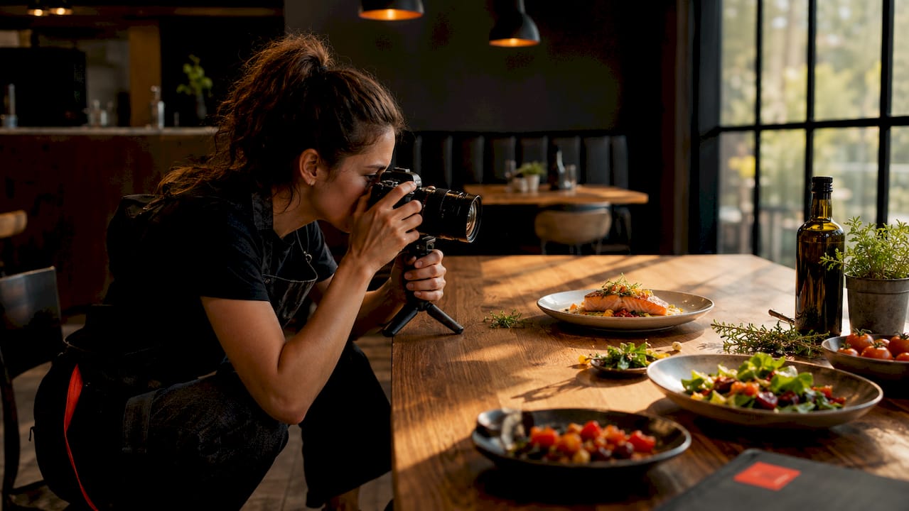 Best practice foto piatti social media per PMI 2 Una food stylist sta scattando delle foto a un piatto di salmone allestito su un tavolo in studio.