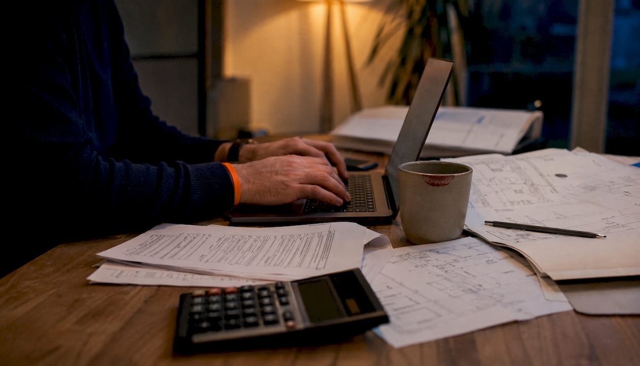 Hands typing laptop among budget documents
