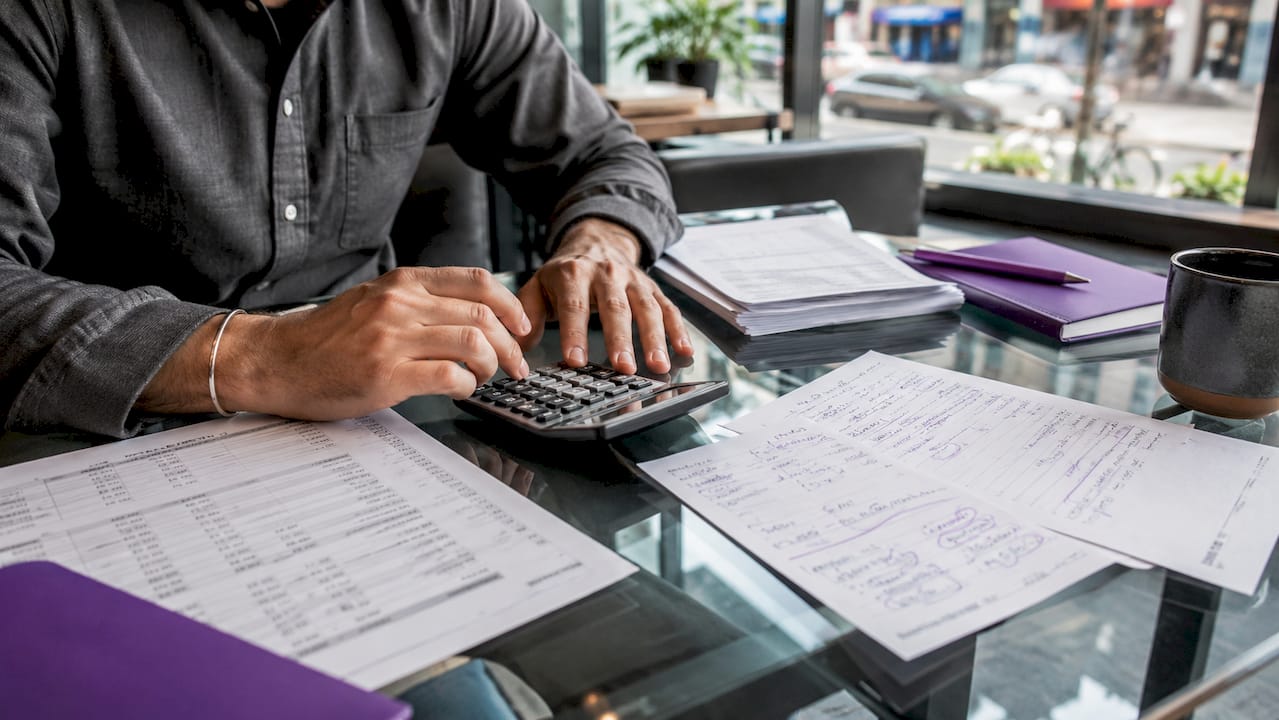Hands using calculator to reconcile ledger records