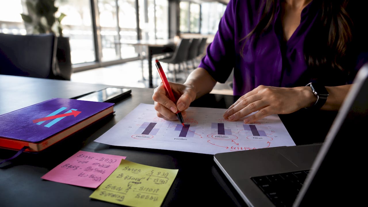 Hands annotating trading metrics on paper