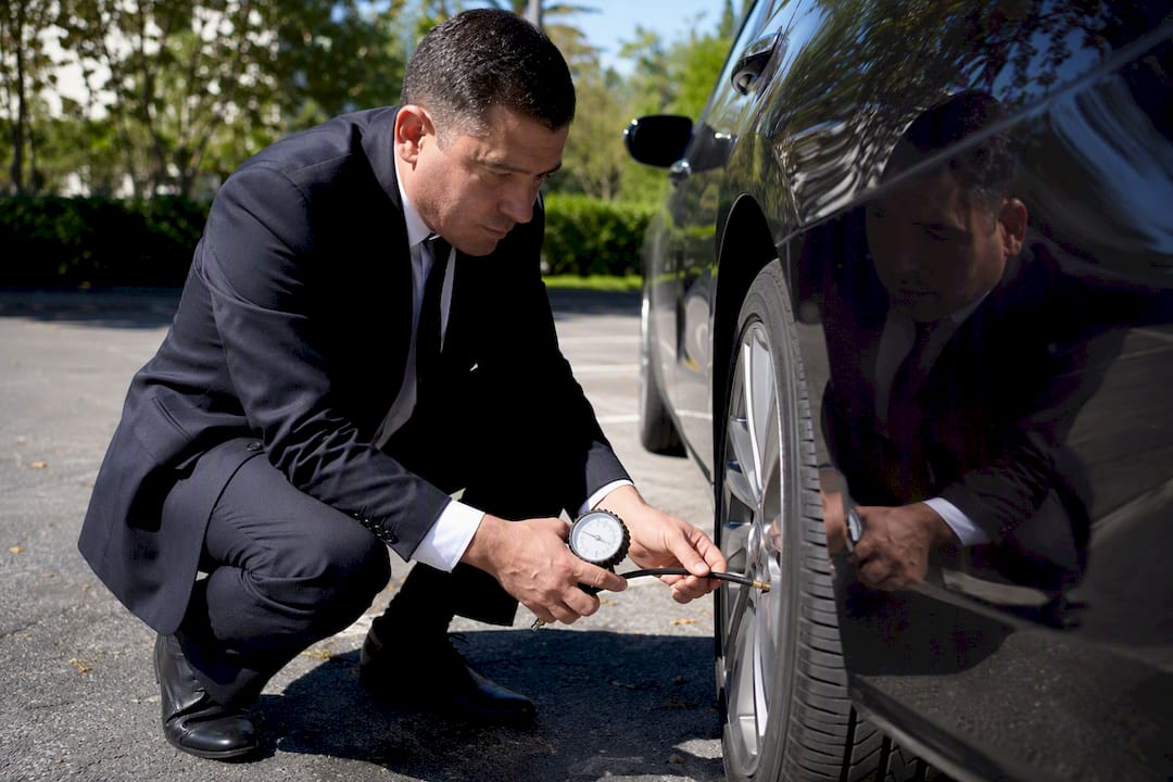 Chauffeur inspecting luxury vehicle tire safety
