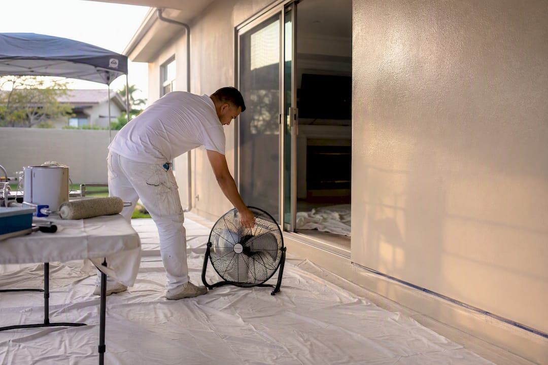 Hands adjusting fan near open window for ventilation