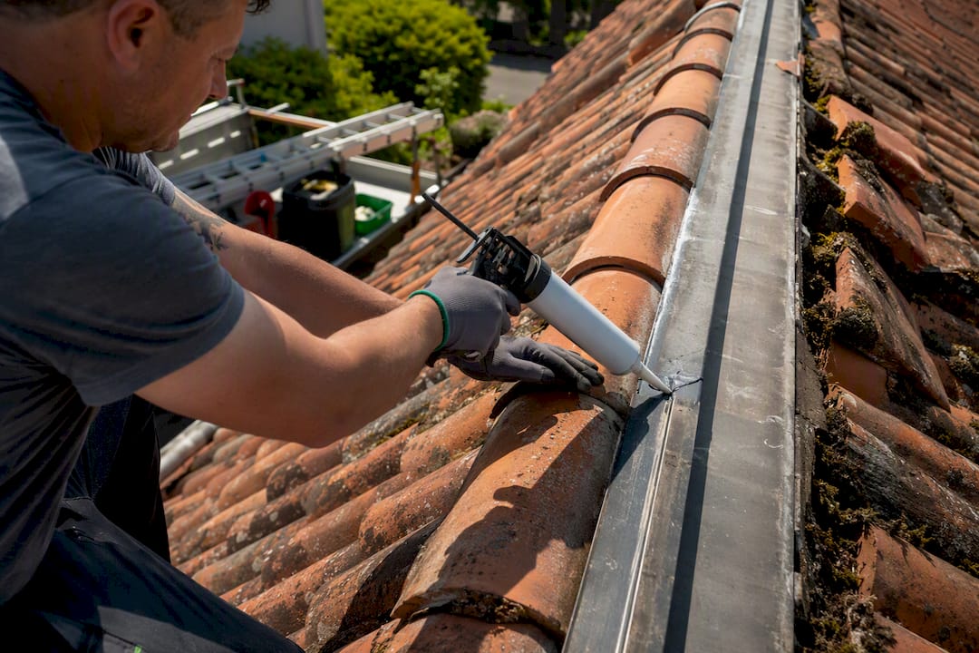 Hands applying sealant to roof flashing