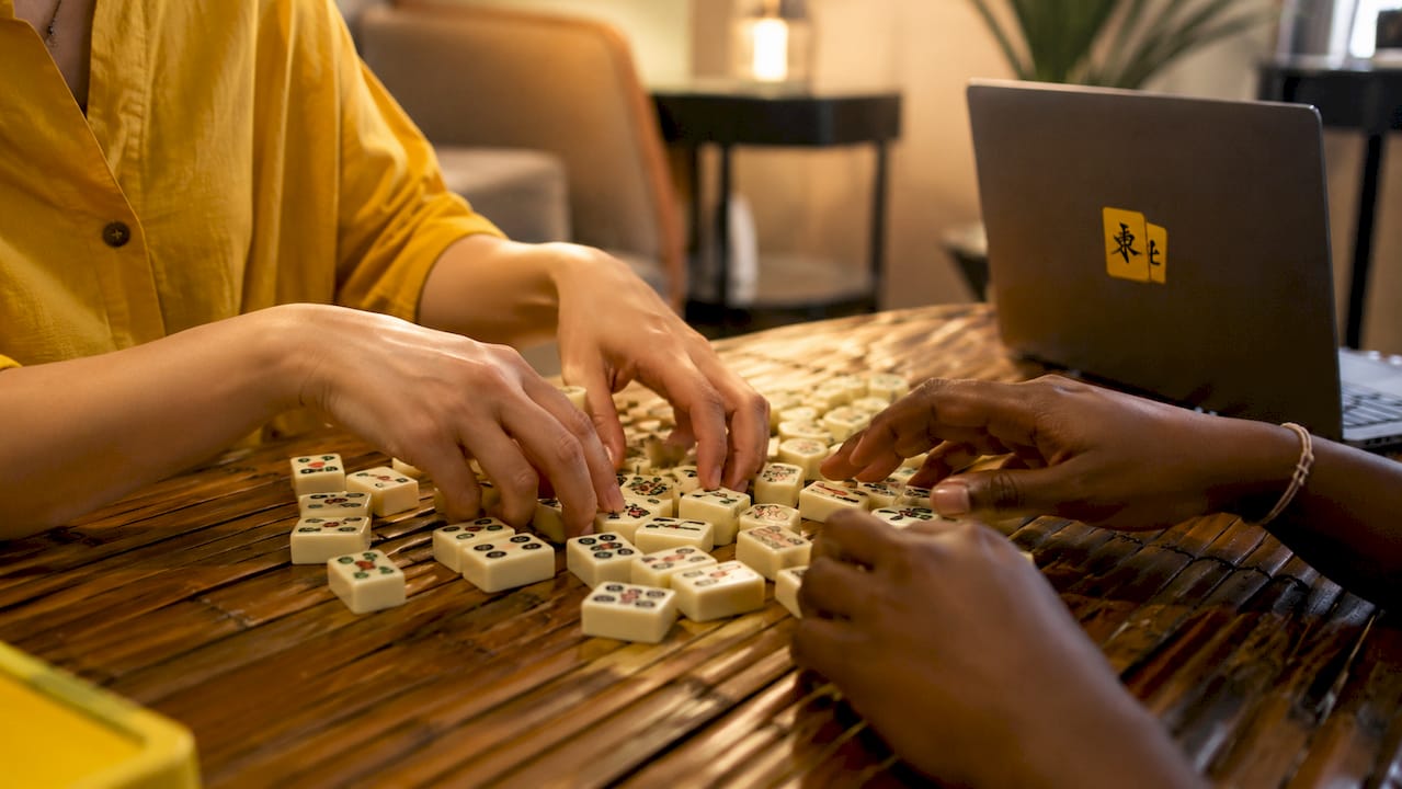 Hands shuffling mahjong tiles on wooden table