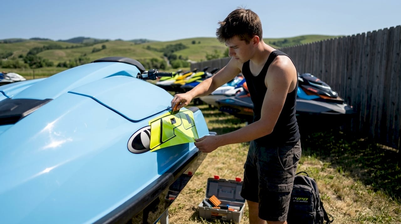 Applying yellow-green vinyl decal on jet ski hull