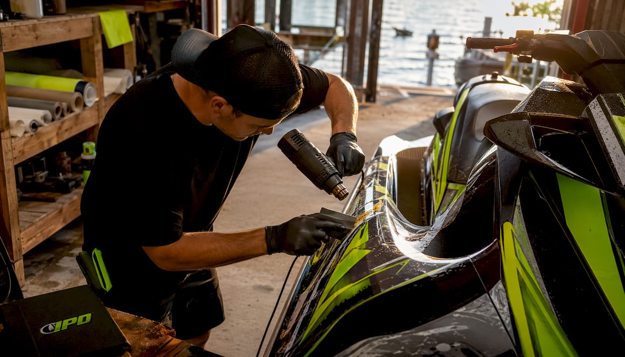 Hands maneuvering vinyl on PWC hull seam installation