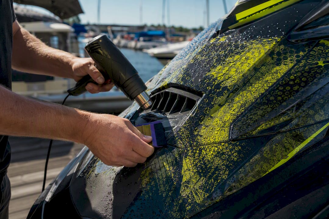 Hands sealing vinyl wrap edges on jet ski intake