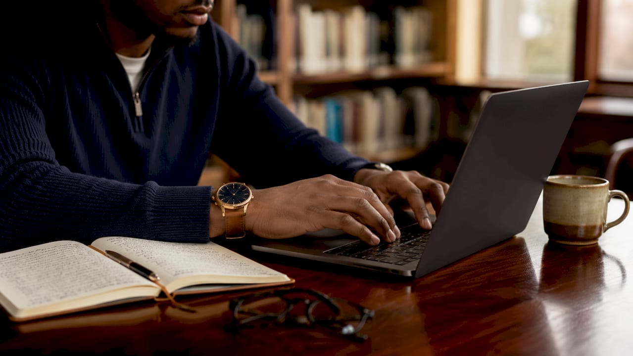 Hands typing on laptop in library study room