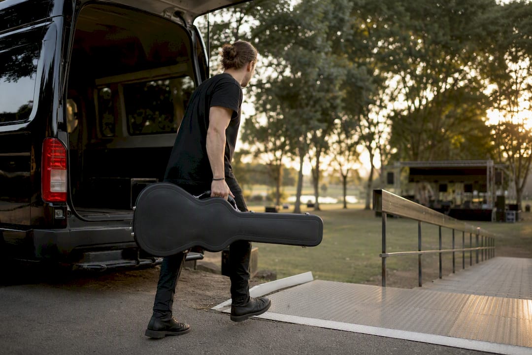 Person carrying guitar case up stairs from van