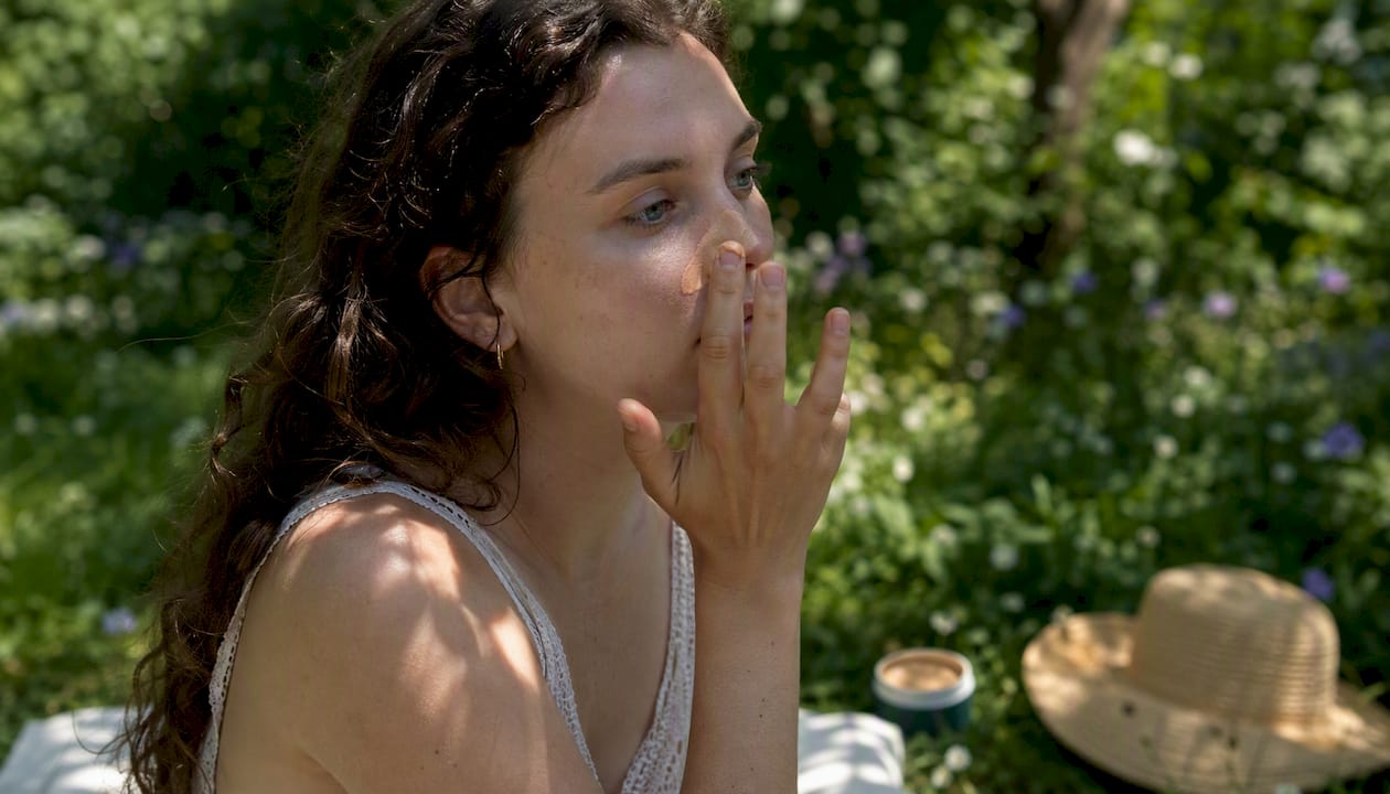 Woman applying tinted mineral sunscreen on face outdoors