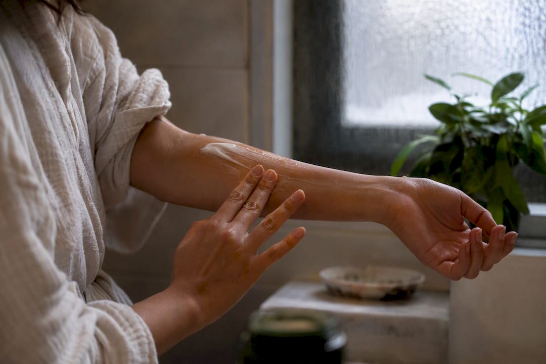 Hands applying balm in soft-lit bathroom in evening
