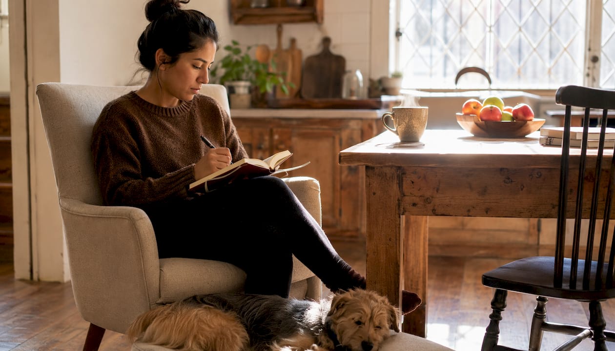 Owner journaling beside anxious dog indoors