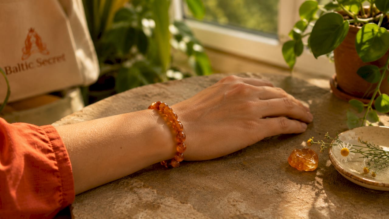 Wrist wearing amber bracelet with amber stone nearby