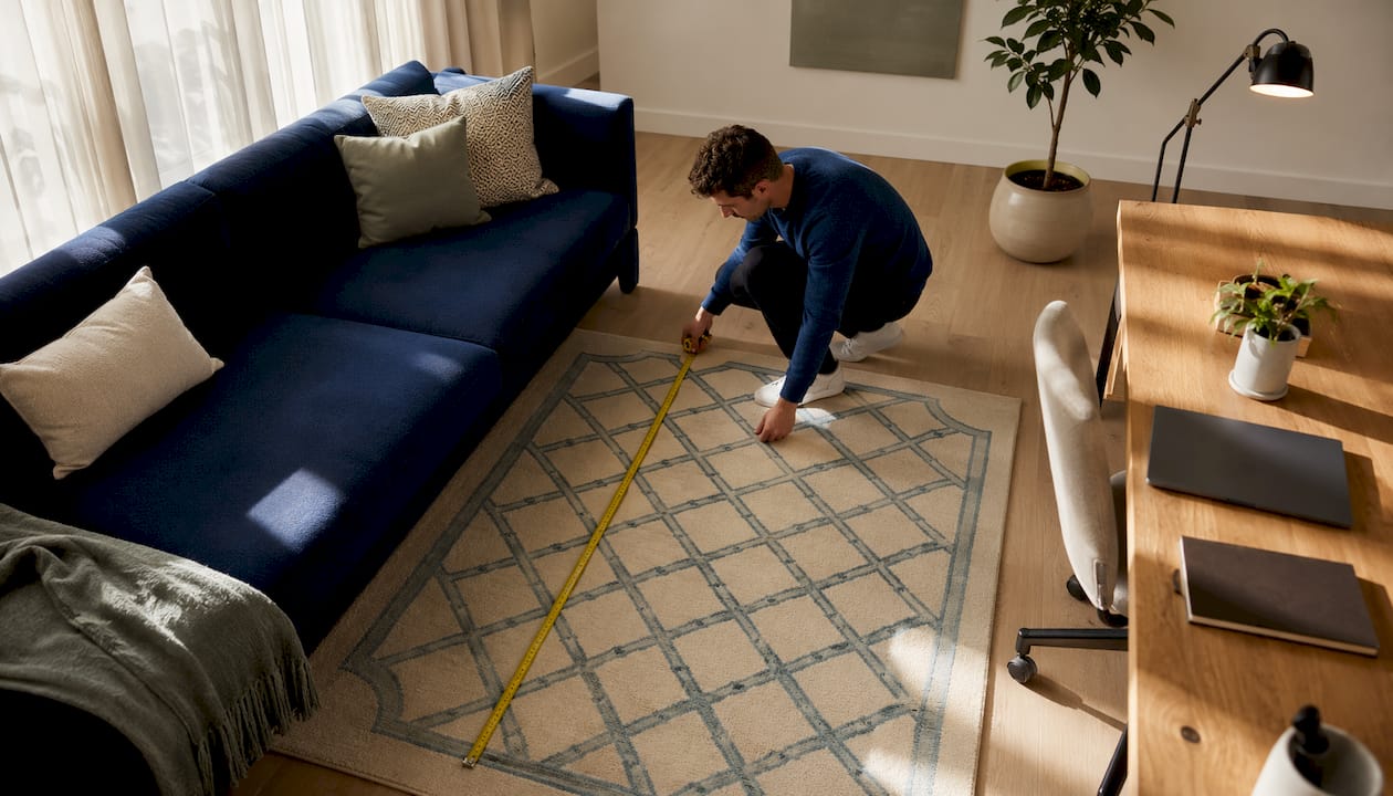 Man measuring area rug beside sofa