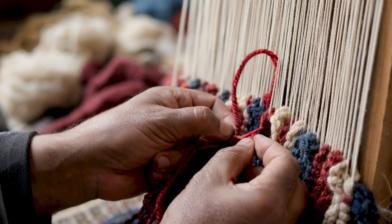 Hands tying knots on wool pile rug