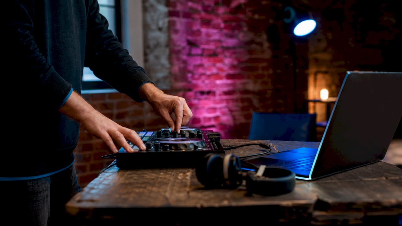 Detailopname van handen die een DJ-controller bedienen, met een laptop ernaast.