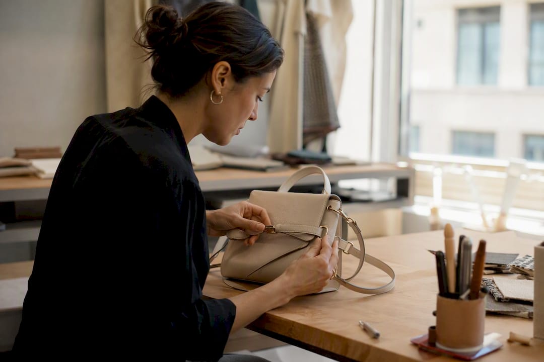 Hands inspecting bag hardware and stitching