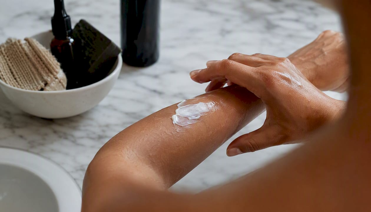 Hands layering lotion and oil on skin