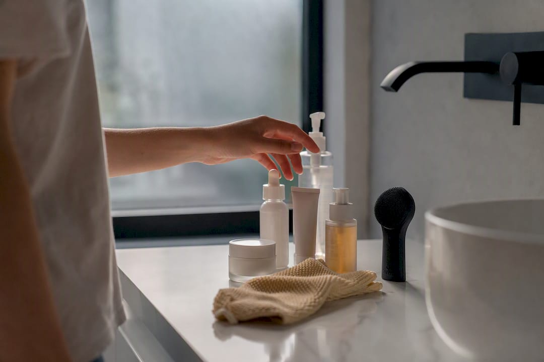 Hand choosing skincare product in bathroom