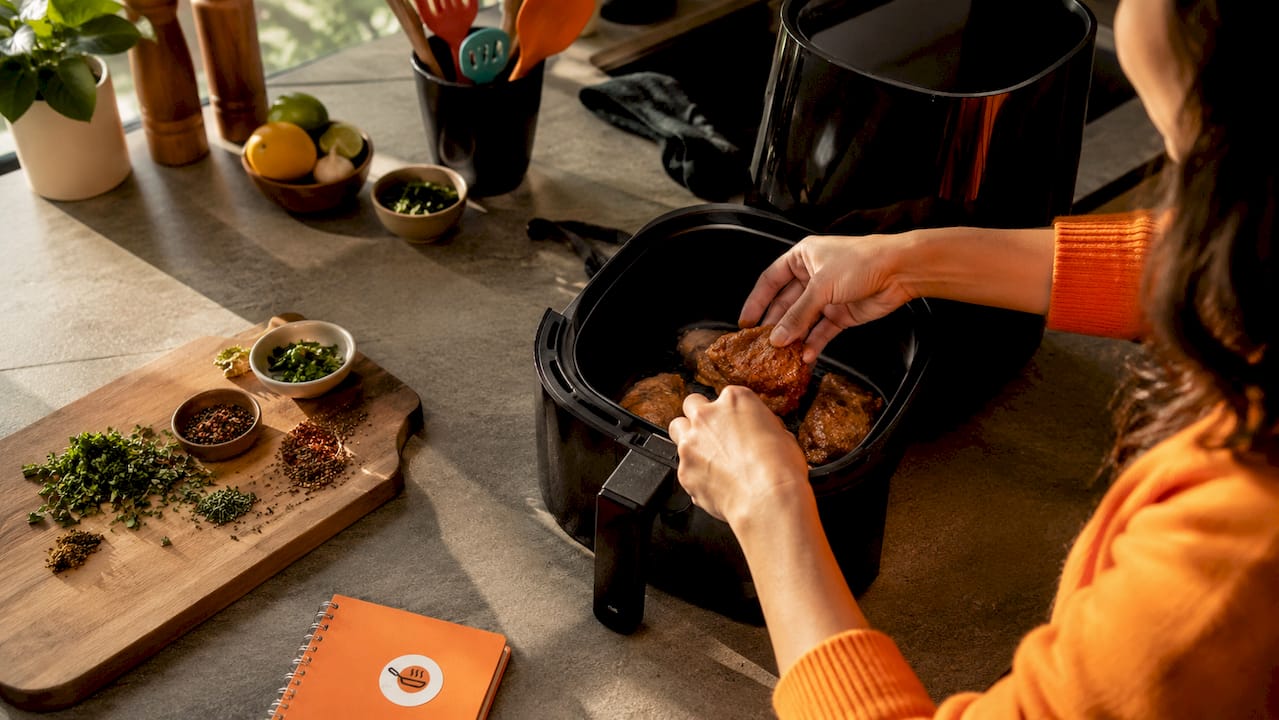 Hands seasoning chicken in air fryer