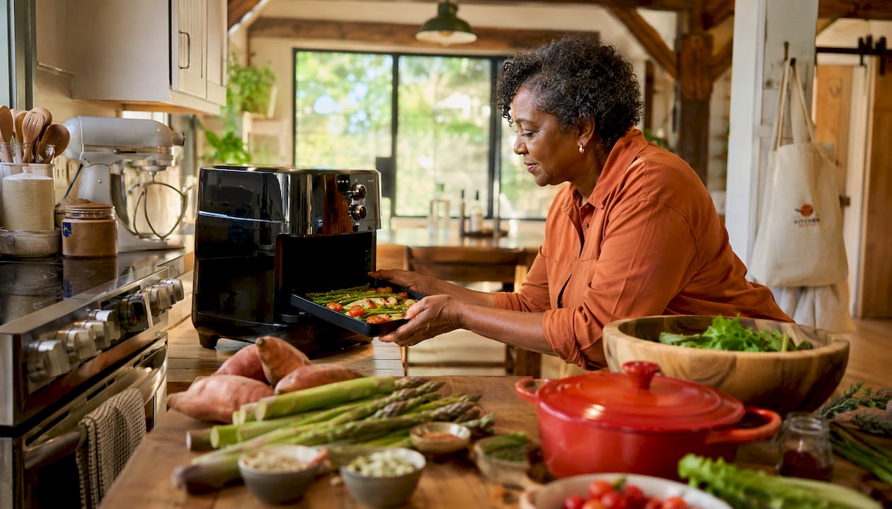 Woman using air fryer with seasonal vegetables in kitchen