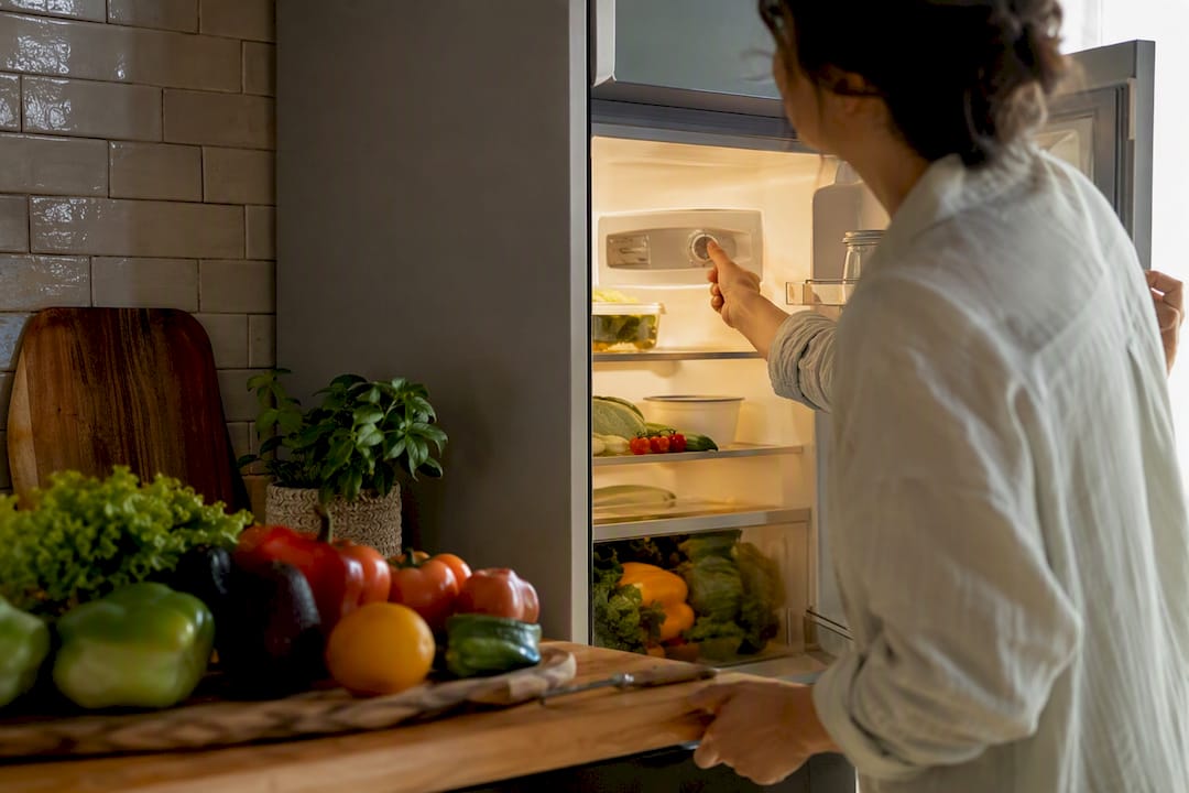 Hand adjusting refrigerator temperature knob inside kitchen