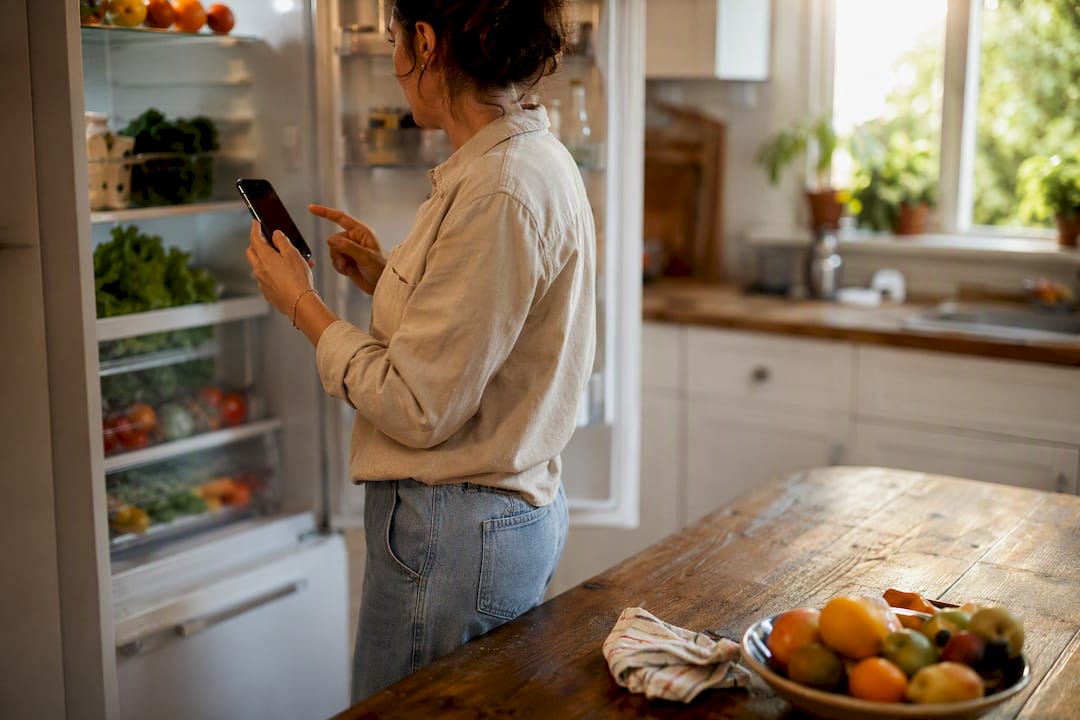 Person checking smart fridge contents on phone