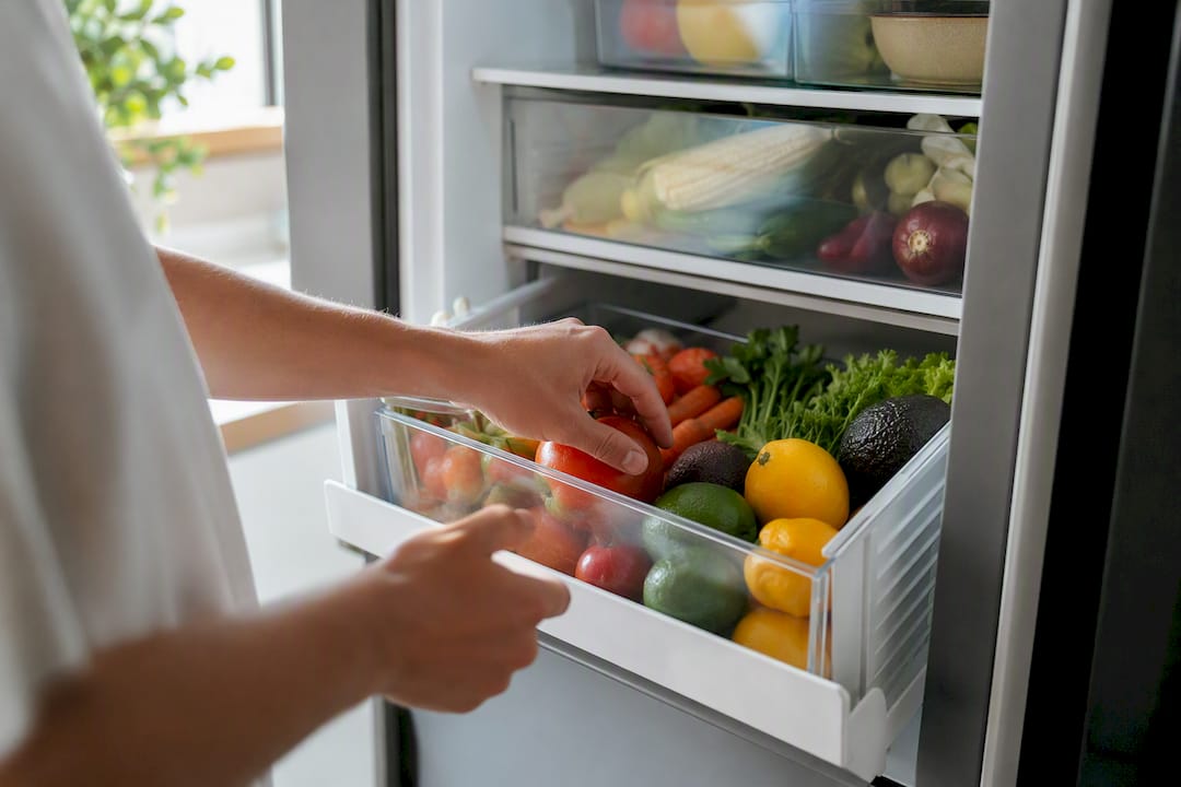 Hands opening fridge drawer with produce