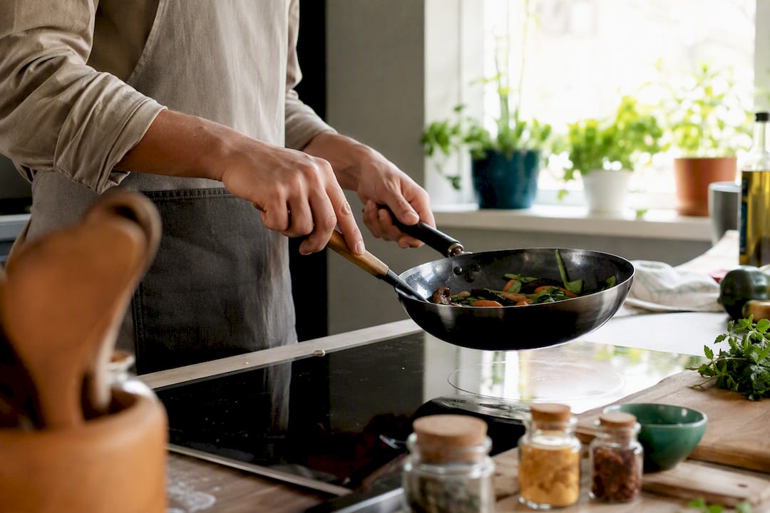 Hands holding carbon steel pan over induction cooktop