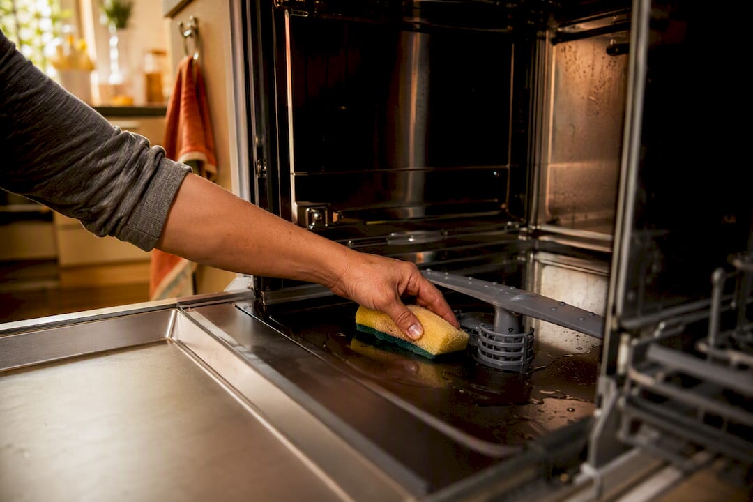 Hands removing water from dishwasher tub