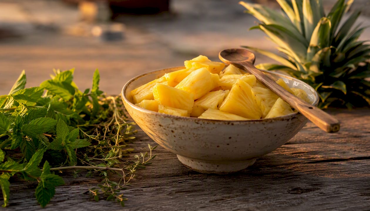 Piña recién cortada en rodajas junto a una cuchara de madera