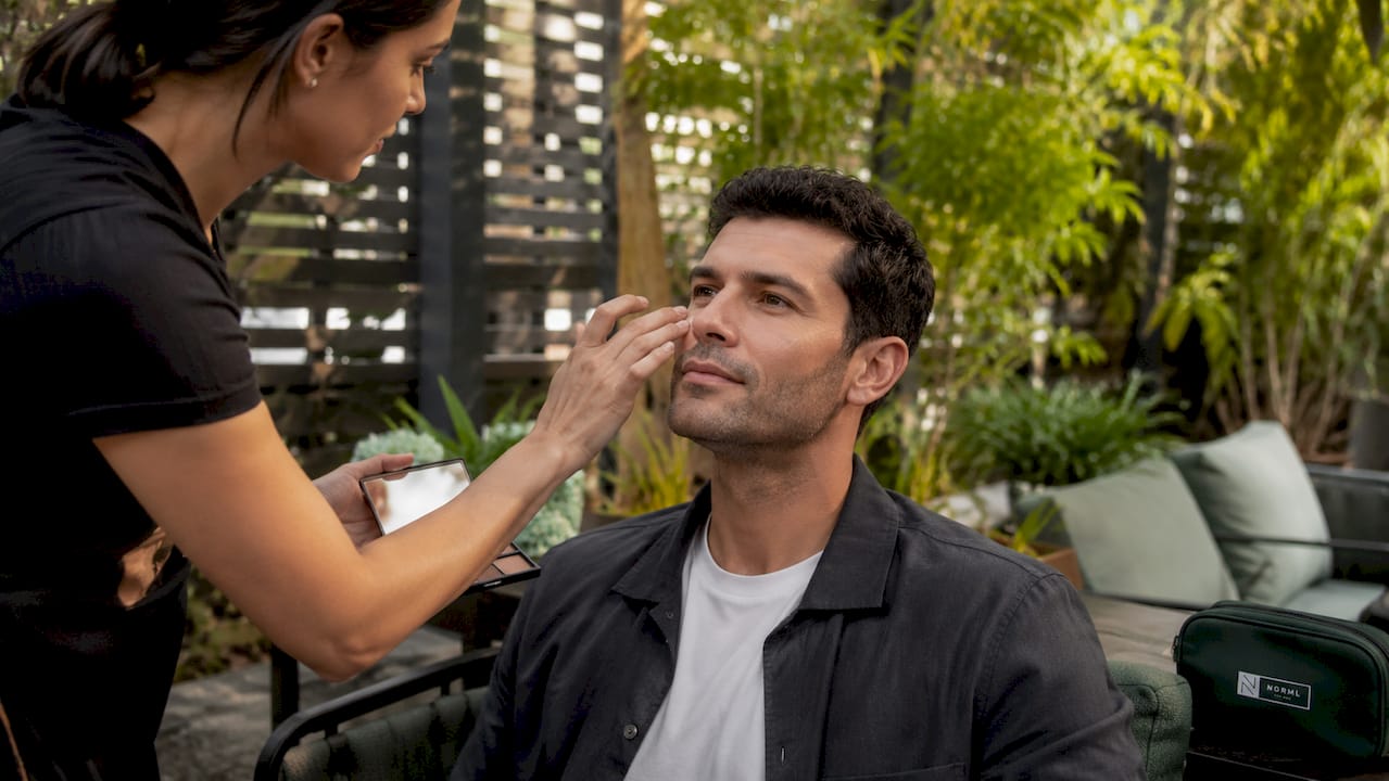 Close-up of hands tapping concealer on male client cheek