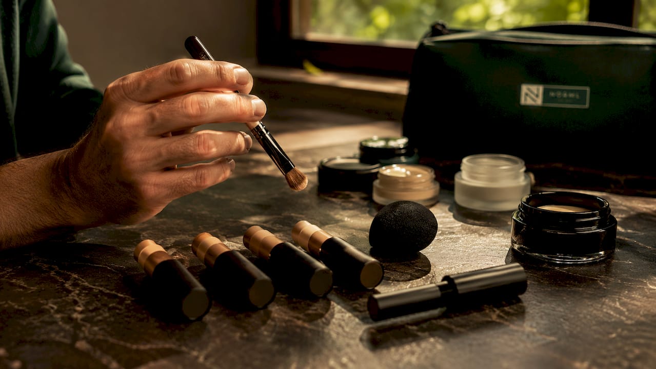 Male hand holding concealer brush and cosmetics