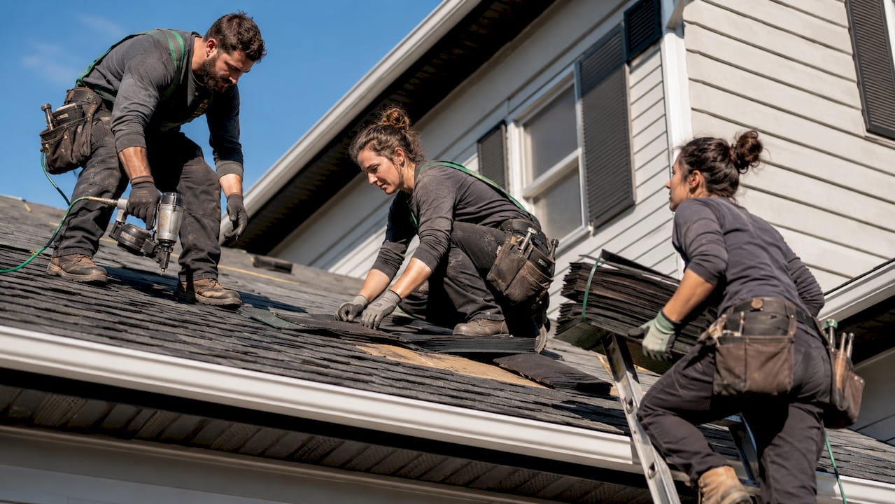 Roof repair team collaboratively replacing shingles outdoors
