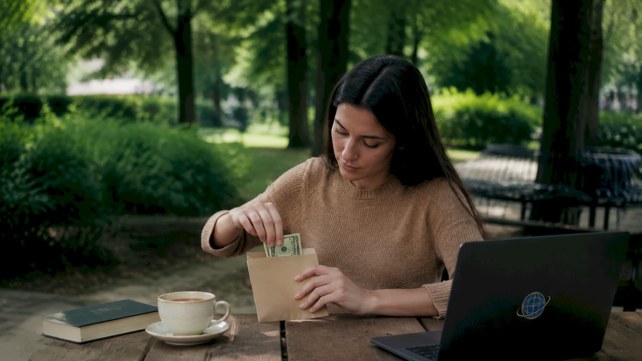 Assise à la terrasse d’un café, une femme effectue son versement mensuel pour son investissement, tout en profitant de l’ambiance chaleureuse autour d’elle.