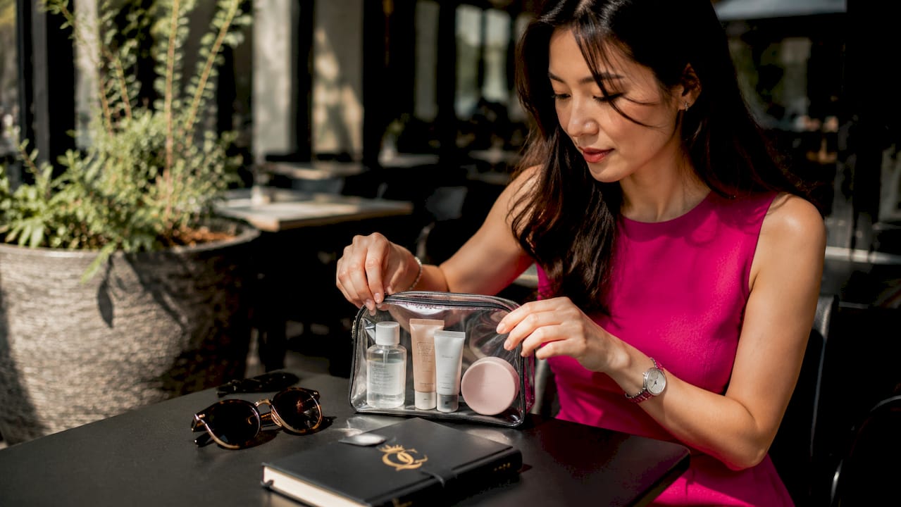 Woman organizing travel skincare kit at desk