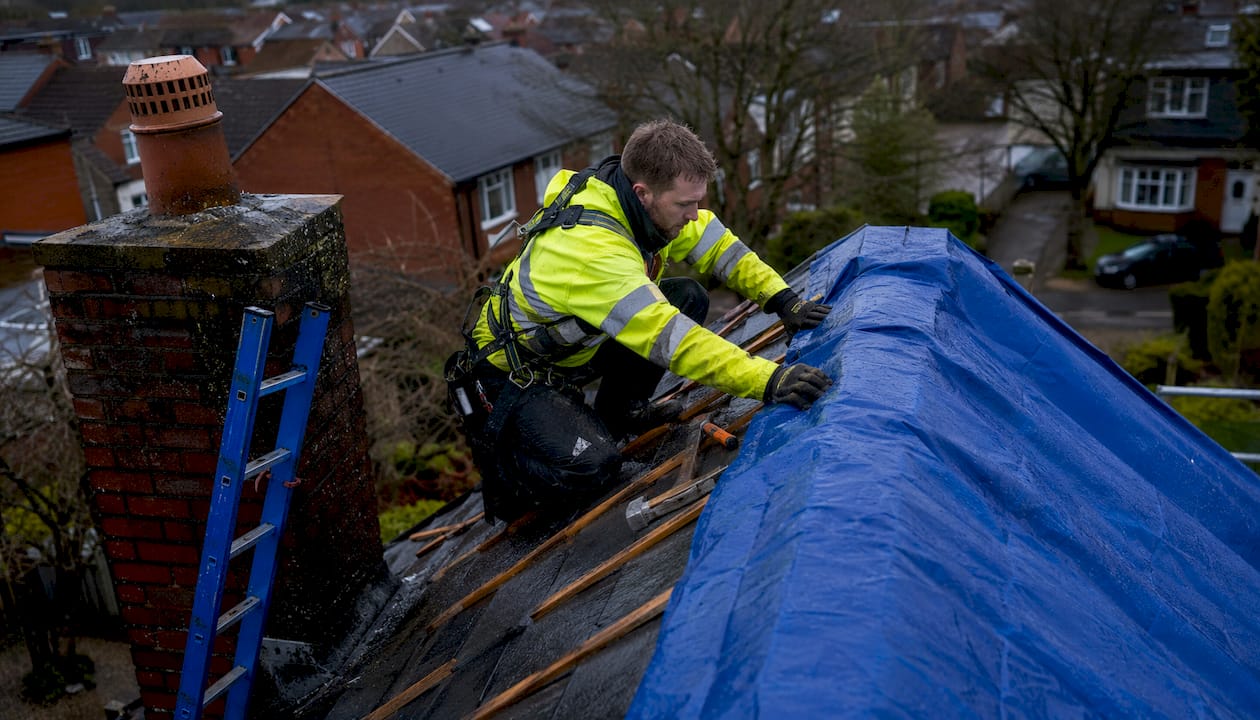 Roofer fitting waterproof tarp on pitched roof