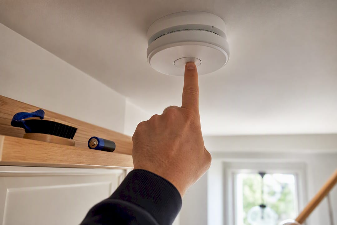 Hand testing ceiling-mounted smoke alarm