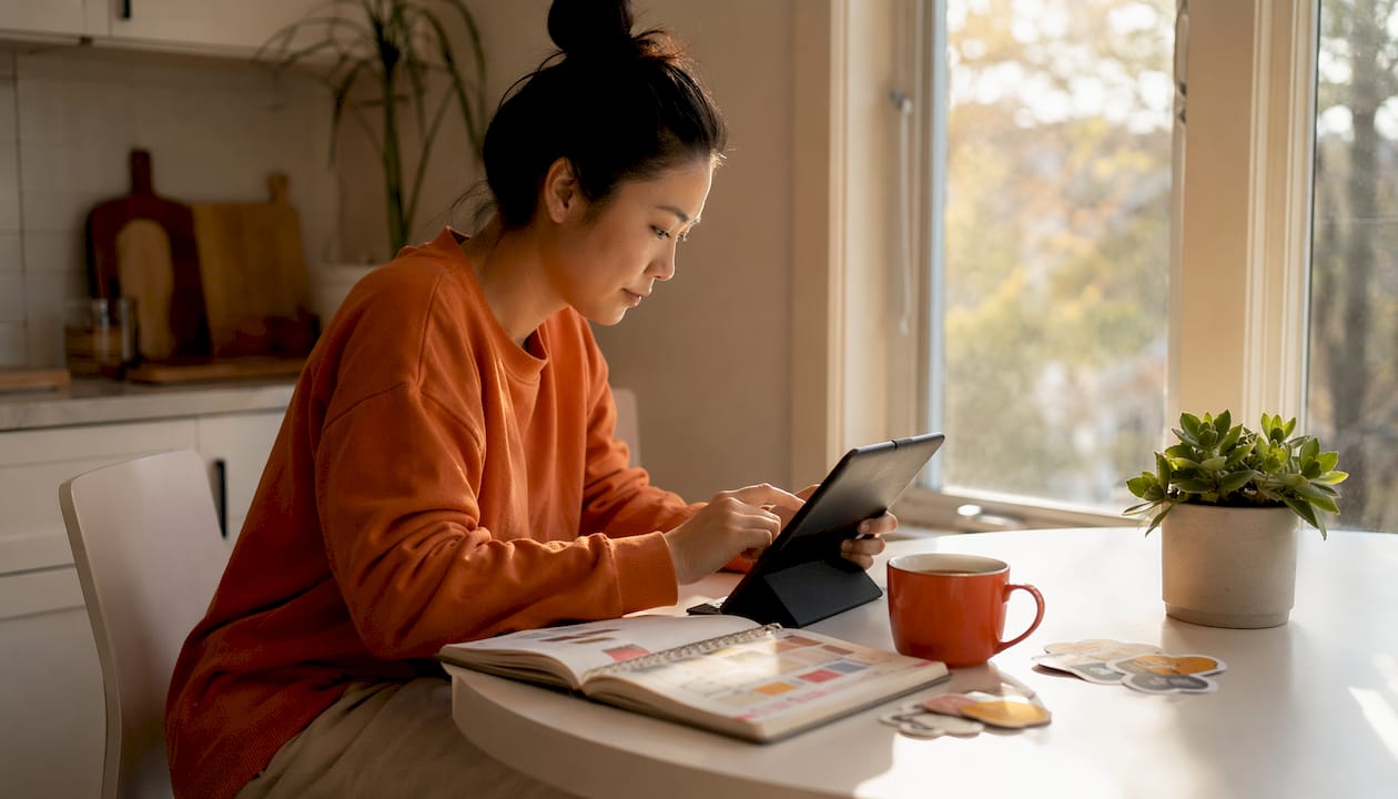 Hands holding smartphone over laptop and design sketches