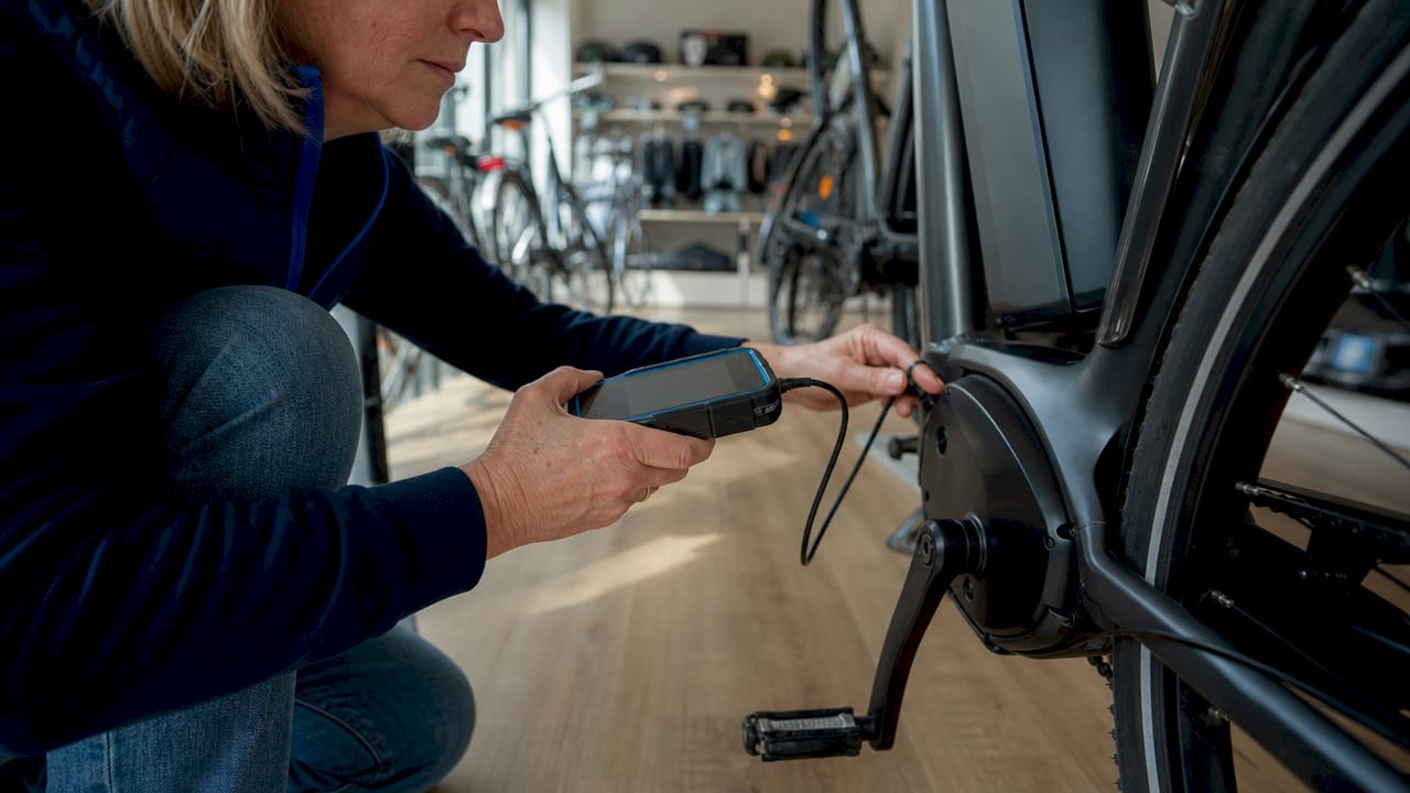 Vrouw inspecteert motor van e-bike in fietsenwinkel
