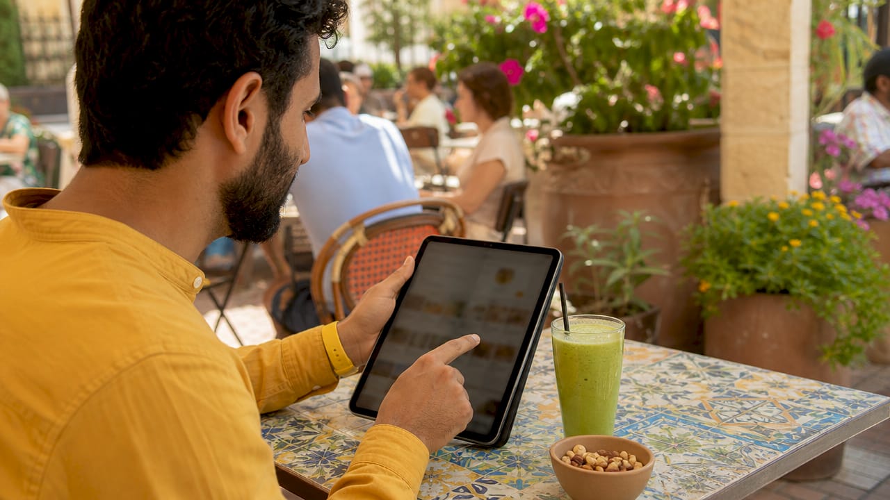 Hands selecting snacks on tablet at café table outdoors