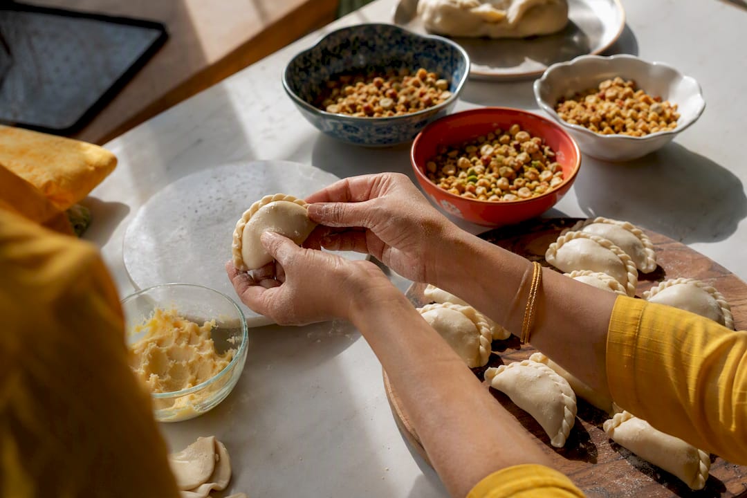 Hands folding gujiya sweets in home kitchen