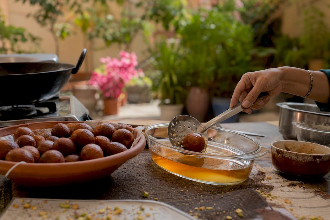 Hand placing fried gulab jamun into syrup bowl