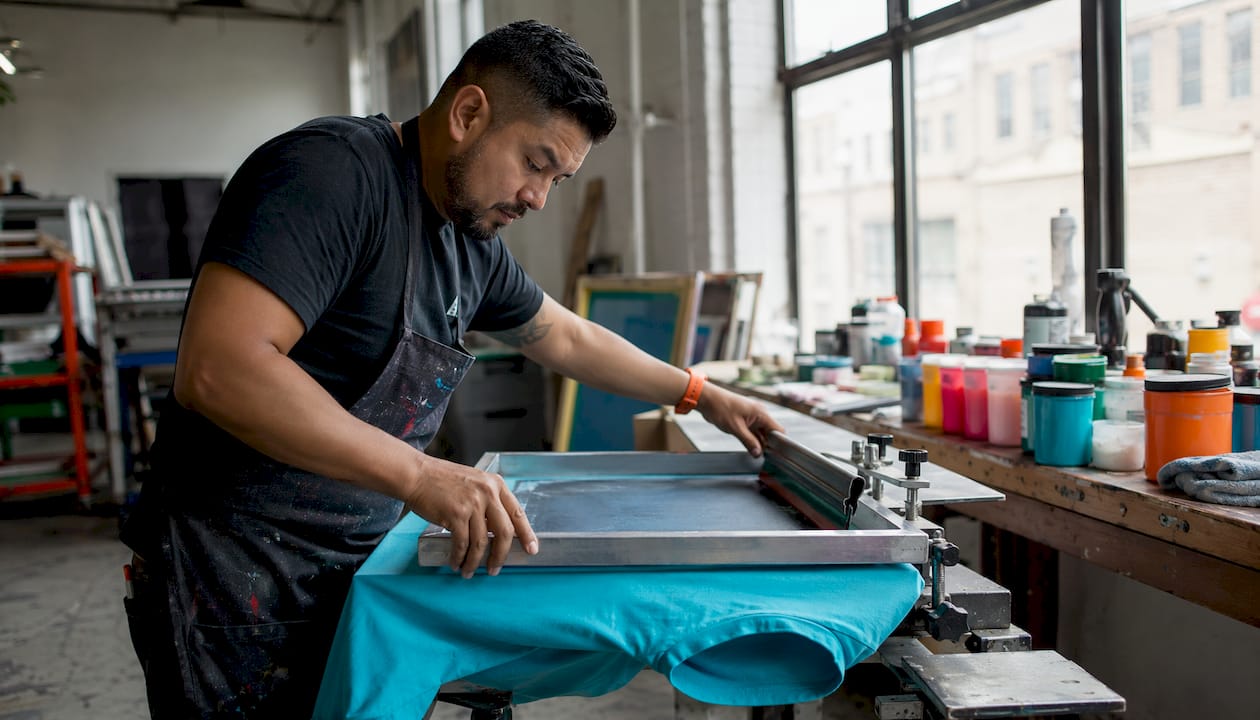 Hands performing screen printing on white T-shirt