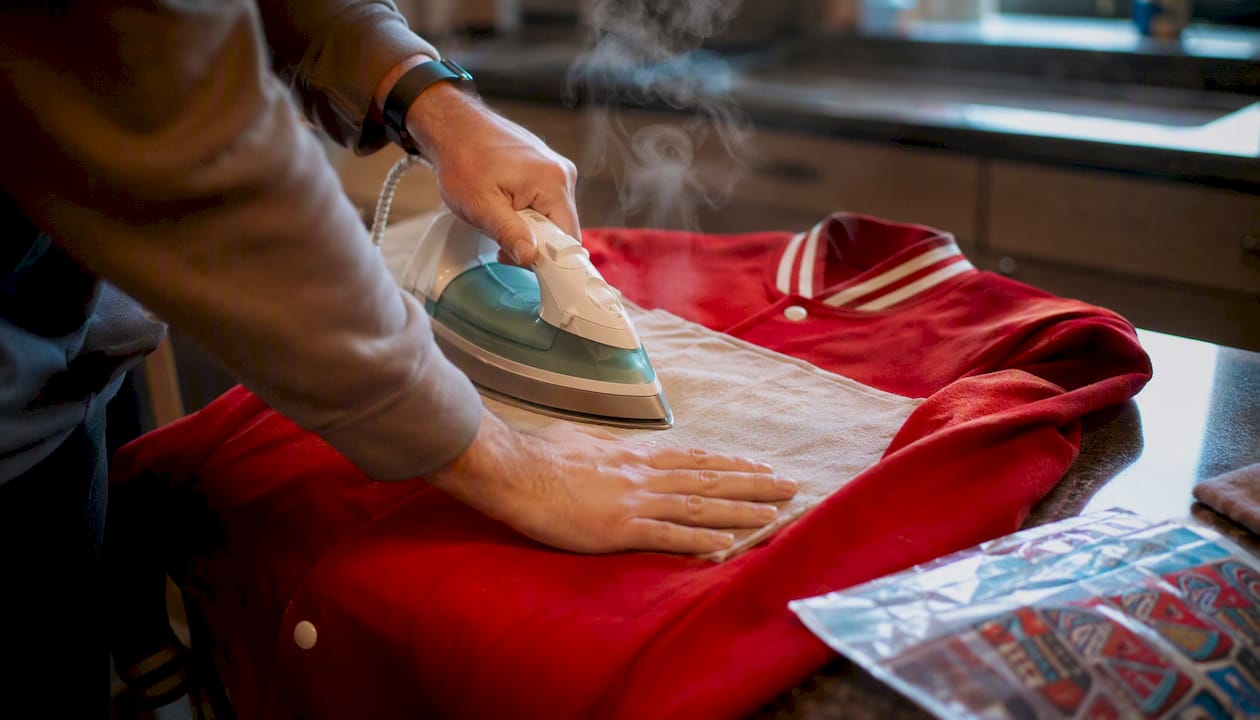 Hands applying iron-on patch on jacket with iron