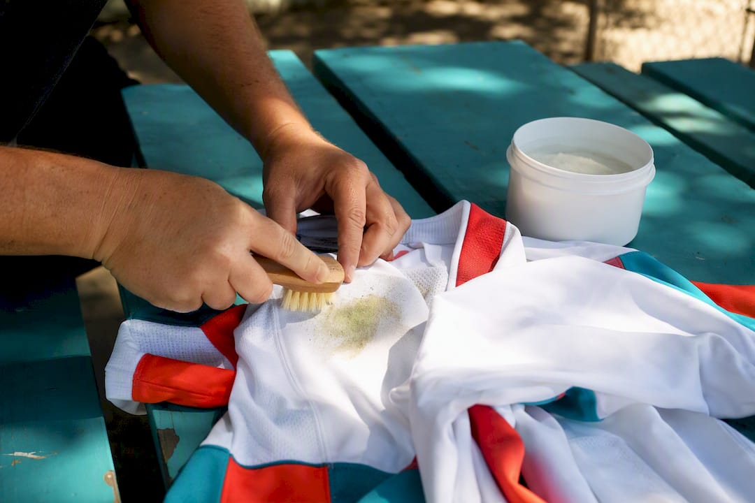 Hands brushing grass stain on colorful sports jersey