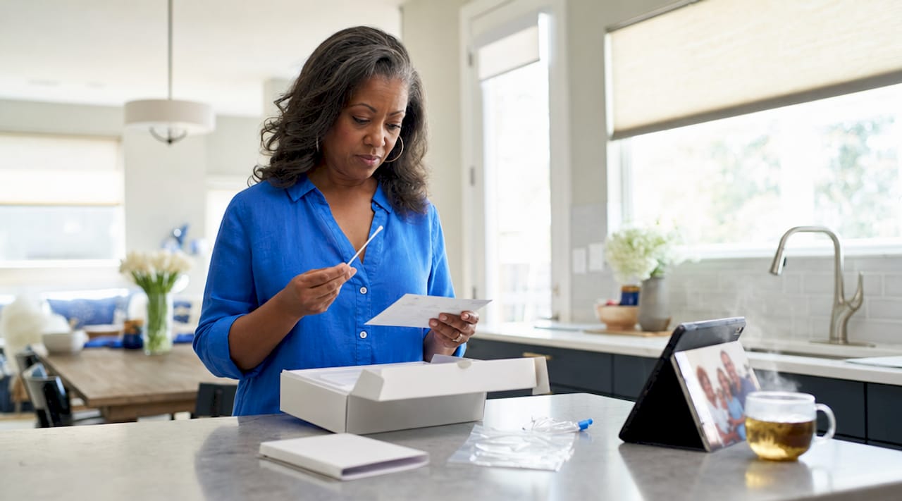 Woman unpacking home DNA test kit at kitchen table