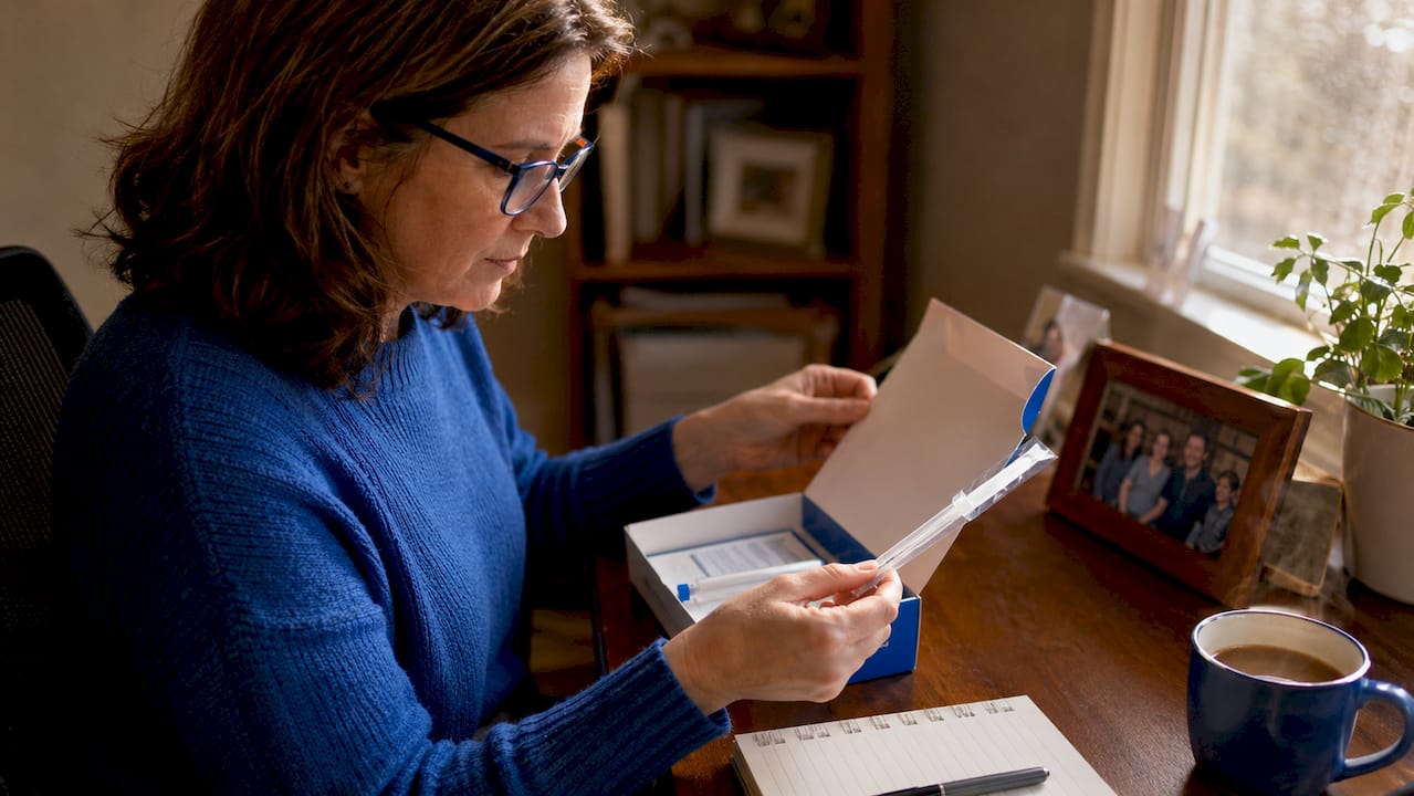 Woman preparing home DNA test kit at kitchen table