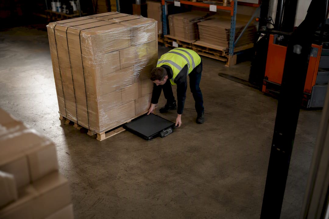Worker weighing loaded pallet on warehouse scale