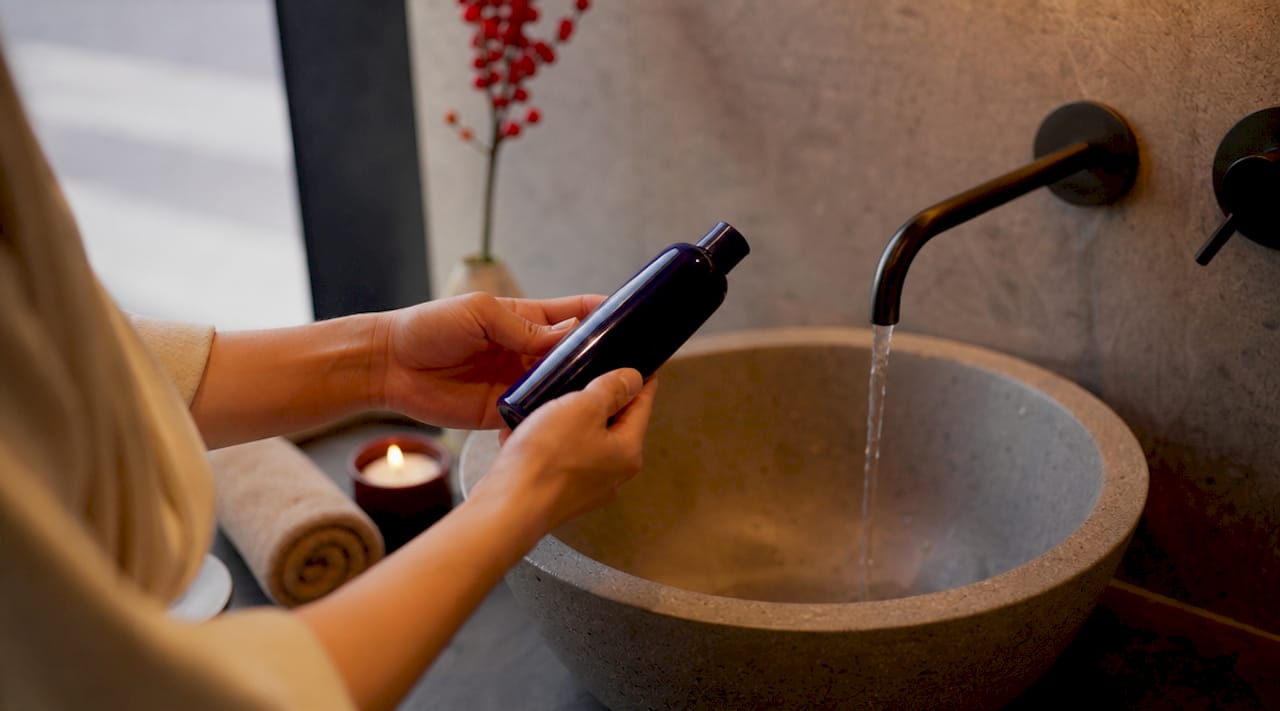 Hands holding sulfate-free shampoo near sink